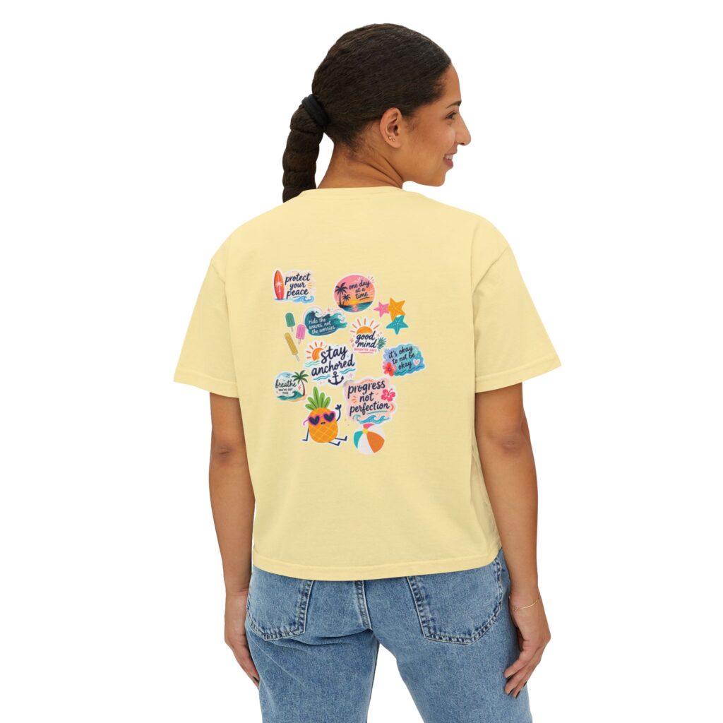 14397025657025562011_2048jpeg - Anchored Back view of a person wearing a pale yellow T-shirt with colorful sticker-style graphics on the back, paired with blue jeans.